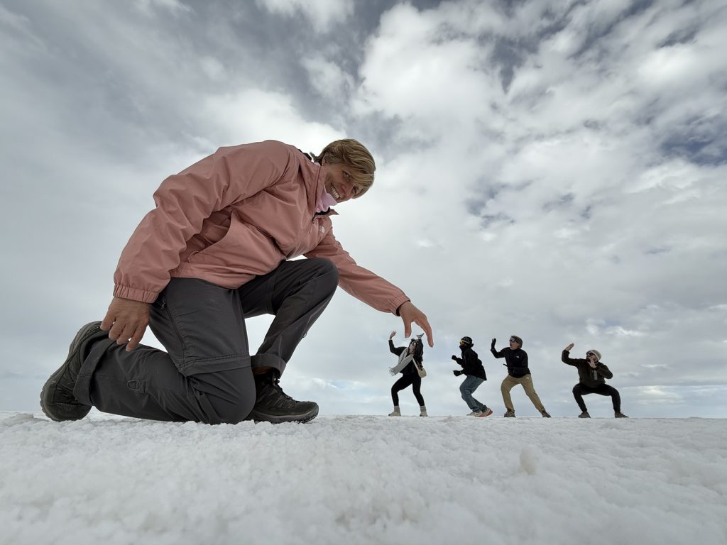 Ruth-practising-slow-travel-in-her-50s-on-the-Salar- de-Uyuni-salt-flats-in-Bolivia-using-forced-perspective-to-appear-giant-against-fellow-travellers-in-the-background